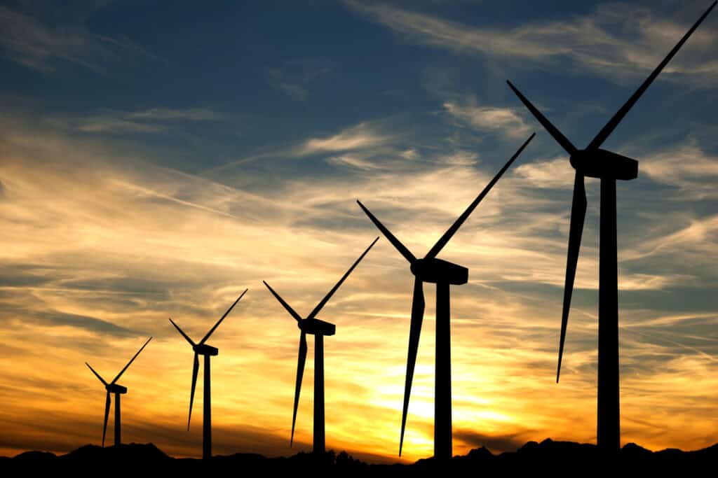 Wind turbines at sunset proving they can be an alternative energy source since solar panels cannot charge at night.