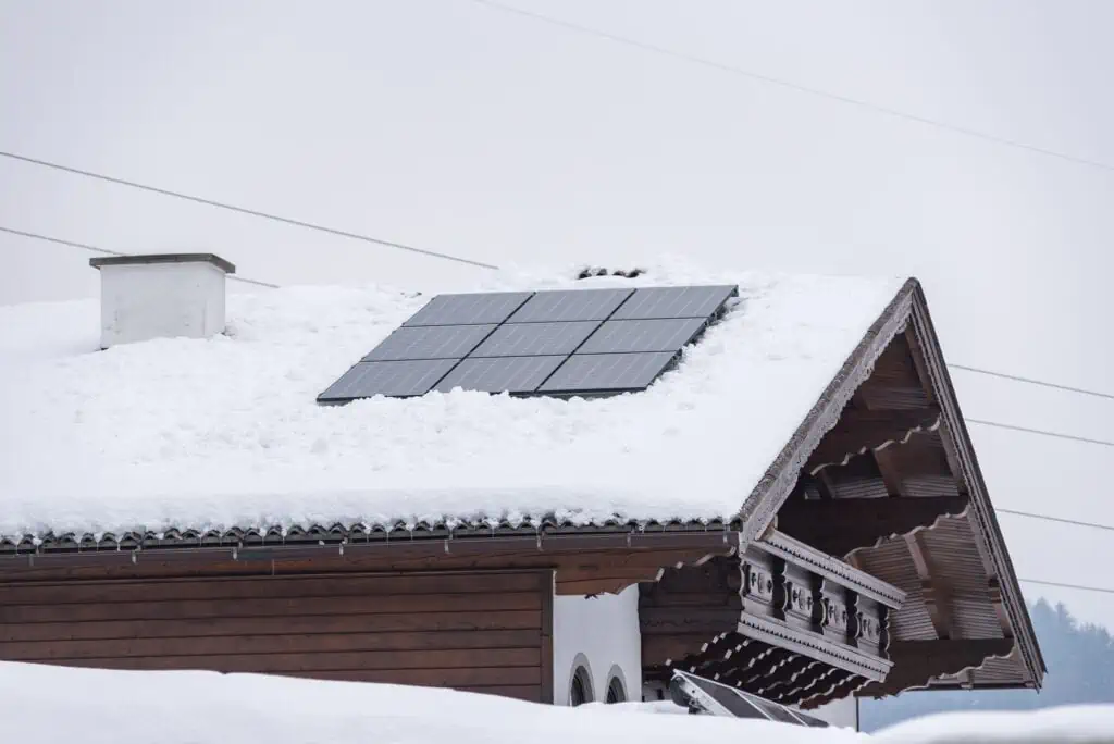 Clean solar panels on top of a snow-covered roof as part of proper insulation practices for solar batteries in cold weather.